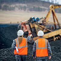 Two miners wearing hard hats pointing to the mine discussing plans