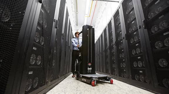 A man stands in a spacious room filled with numerous black servers, highlighting a tech-focused environment.
