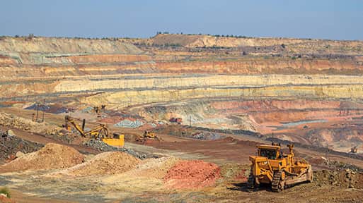 Open-pit mine with terraced extraction levels and heavy machinery.